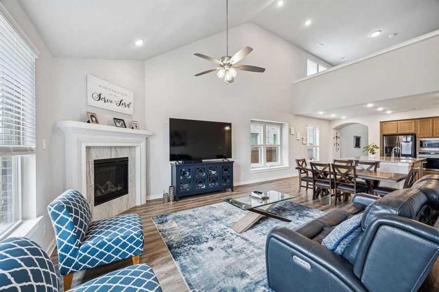 Living room with wood finished floors, a tile fireplace, recessed lighting, high vaulted ceiling, and ceiling fan