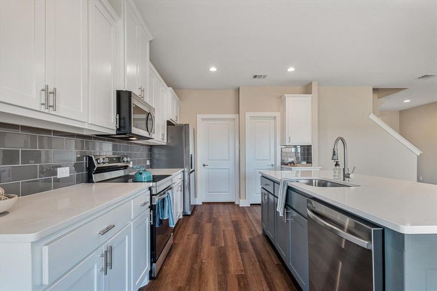 Kitchen featuring stainless steel appliances, dark wood-type flooring, sink, a center island with sink, and white cabinetry Kitchen featuring stainless steel appliances, dark wood-type flooring, sink, a center island with sink, and white cabinetry