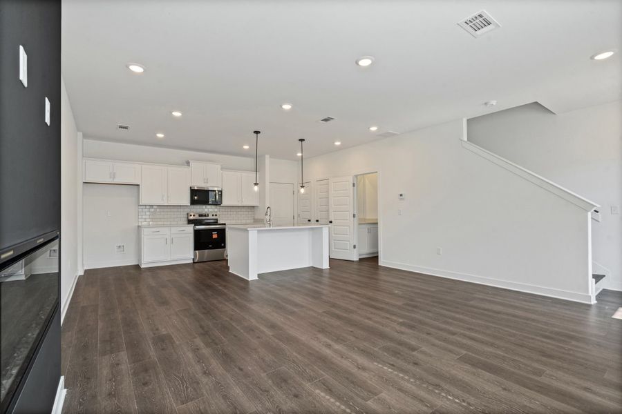 Open-concept living space featuring wood-finish flooring, a kitchen island with pendant lighting, white shaker cabinetry, and a subway tile backsplash Open-concept living space featuring wood-finish flooring, a kitchen island with pendant lighting, white shaker cabinetry, and a subway tile backsplash
