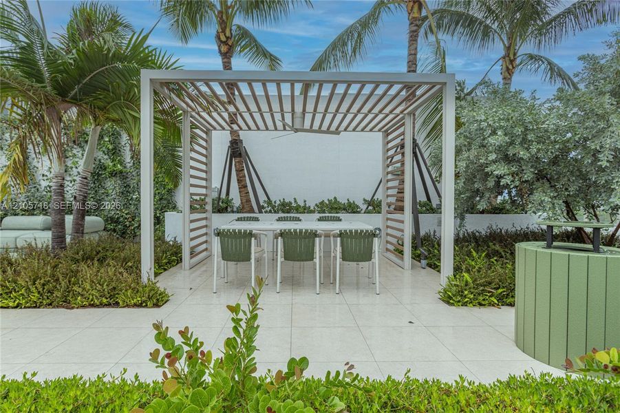 Outdoor patio featuring white tile flooring, a structured wooden pergola with an integrated ceiling fan, and surrounding tropical landscaping