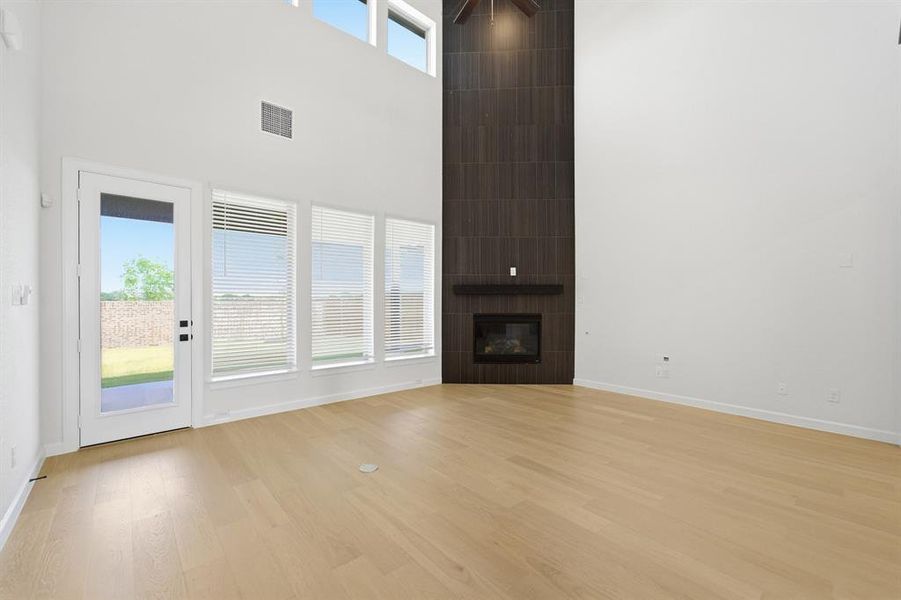 Two-story living area featuring a dark-tiled fireplace with a wood mantel, light wood-finish flooring, and a ceiling fan