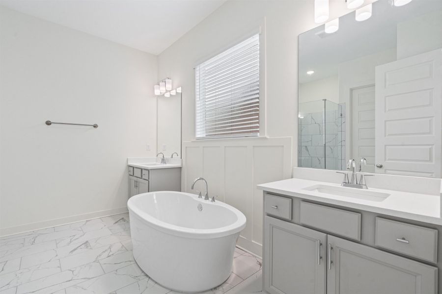Full bath featuring two vanities, a freestanding bath, a marble finish shower, and light marble finish flooring
