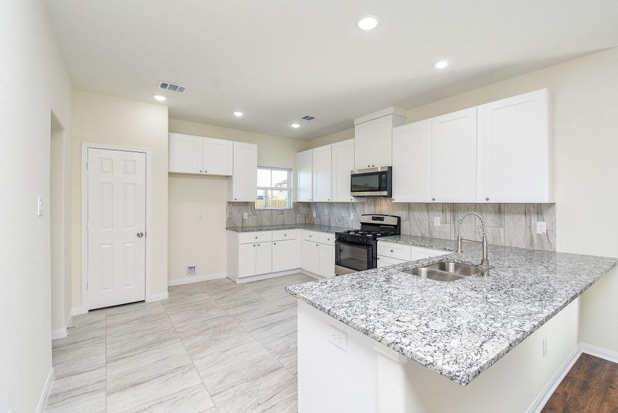 Modern kitchen interior with white cabinetry, stainless steel appliances, and a granite countertop on a central island.