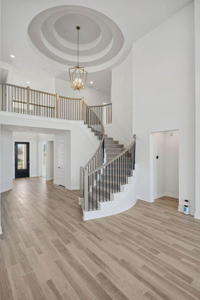 Another view of the foyer showcases the elegant curved staircase with a sleek black wrought-iron and wood railing, while the ceiling features a distinctive circular, multi-tiered design.