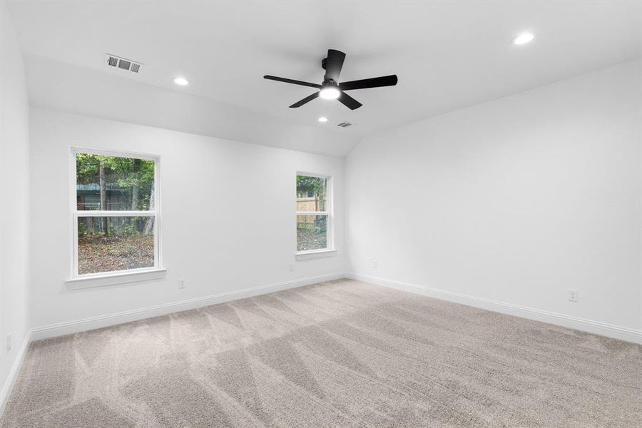 Carpeted spare room featuring vaulted ceiling, ceiling fan, and plenty of natural light