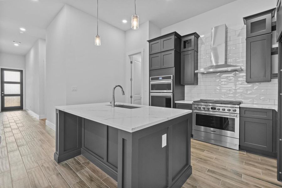 Kitchen featuring decorative light fixtures, sink, appliances with stainless steel finishes, an island with sink, and wall chimney exhaust hood