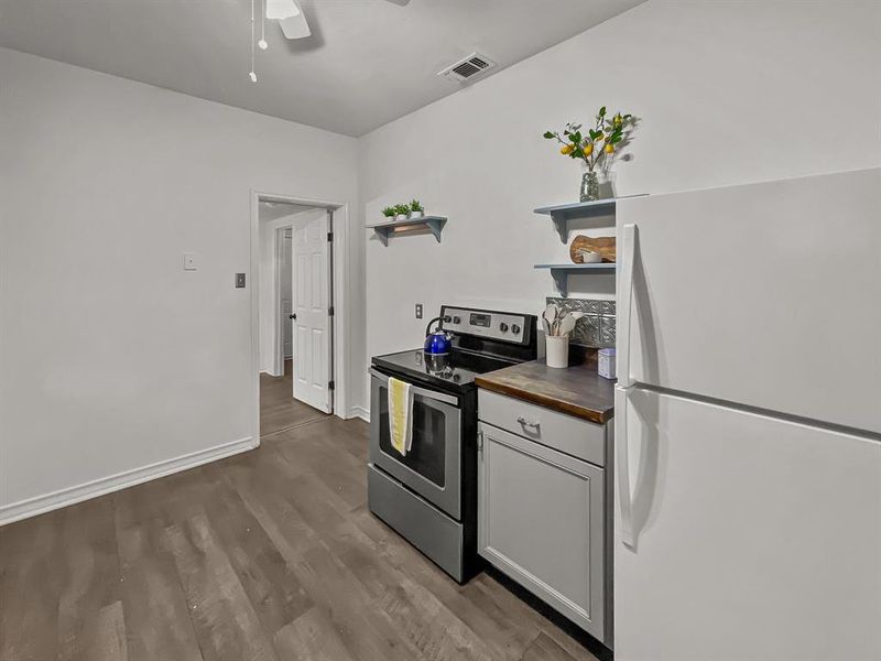 Kitchen featuring wood counters, white refrigerator, dark wood-style floors, stainless steel electric stove, and gray cabinets