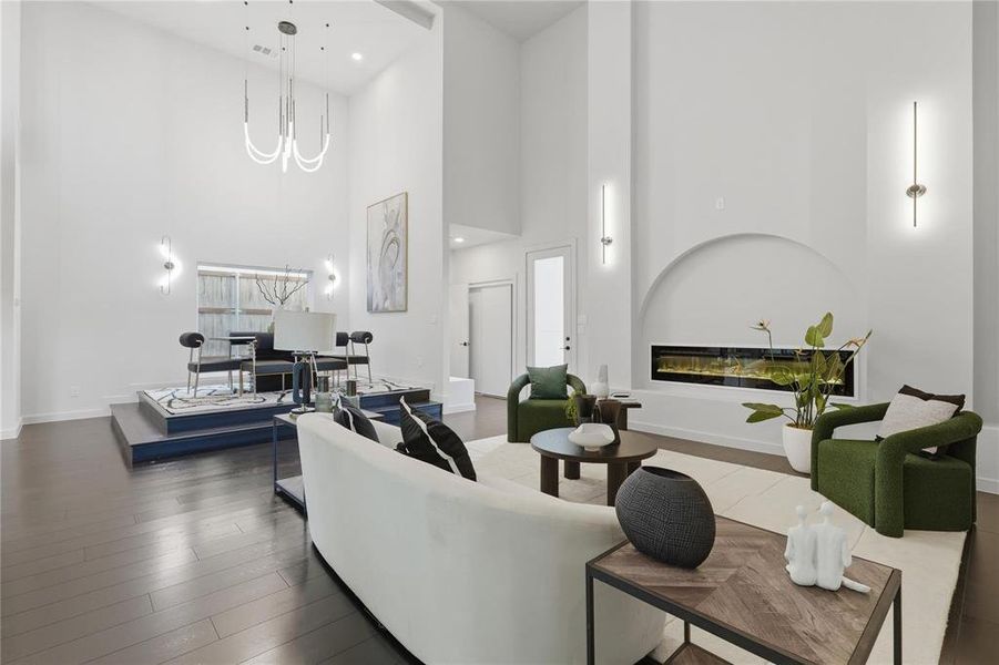 Open-concept living space with dark wood-finish flooring, soaring ceilings, a recessed linear fireplace, and a raised platform area