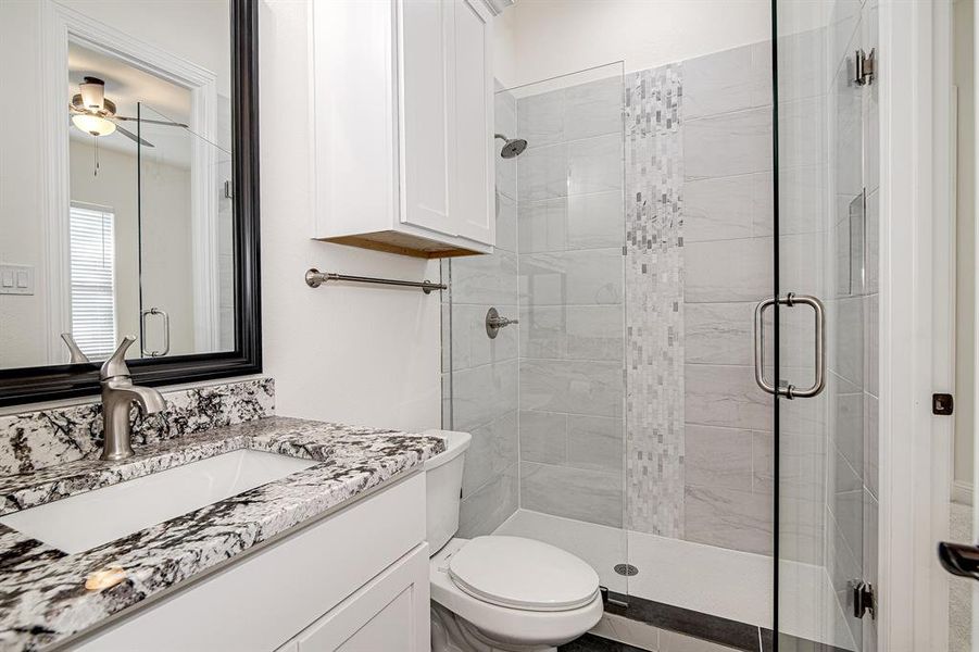 Bathroom with ceiling fan, vanity, a shower with shower door, and toilet