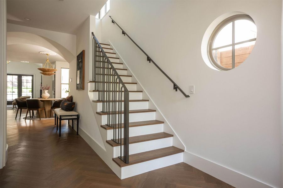 A striking circular window illuminates a clean-lined staircase flanked by herringbone patterned wood floors. A striking circular window illuminates a clean-lined staircase flanked by herringbone patterned wood floors.