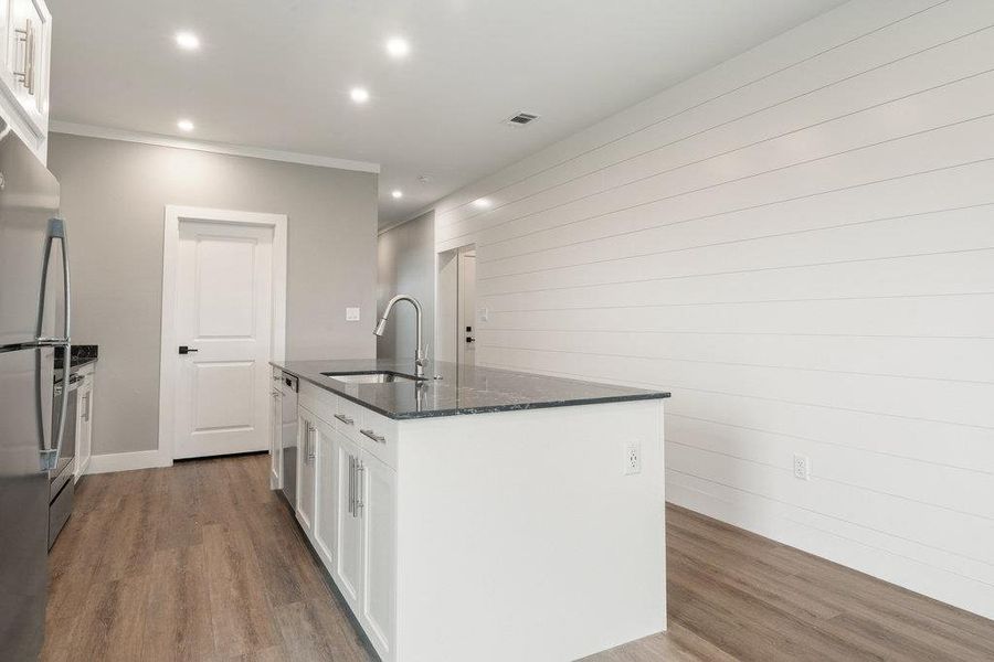 Kitchen with white cabinetry, dark stone counters, dark wood-style flooring, stainless steel appliances, and accent wall