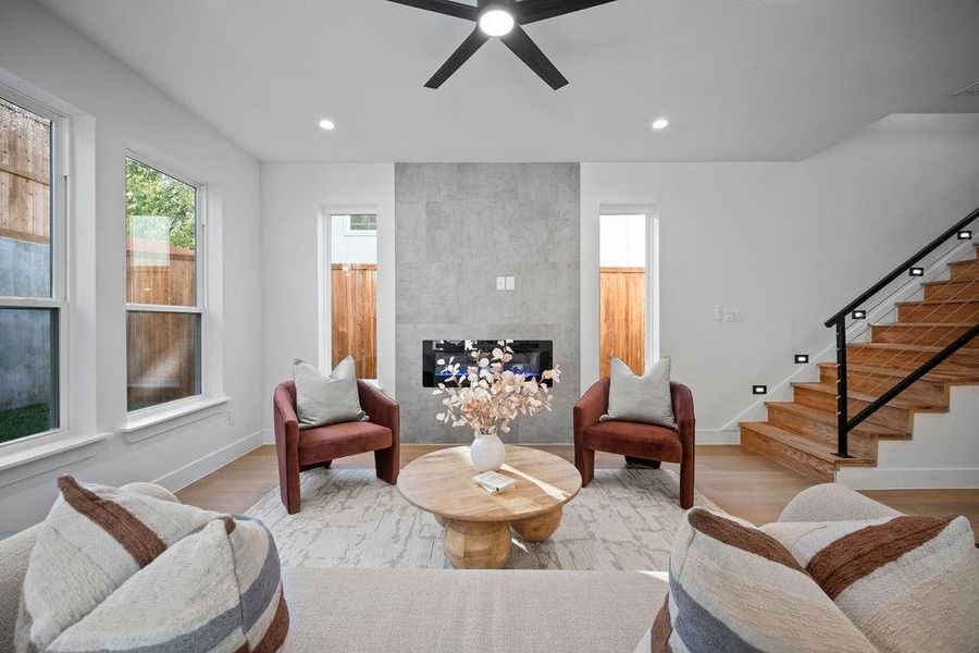 Living room with a tile fireplace, light wood-type flooring, and ceiling fan