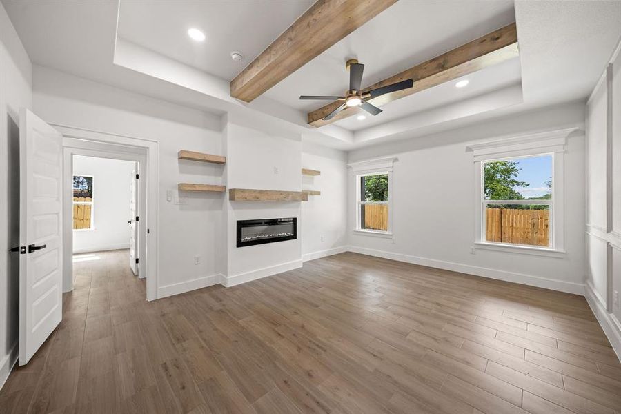 Spacious room featuring wood-finish flooring, a tray ceiling with exposed wood beams, and a modern ceiling fan