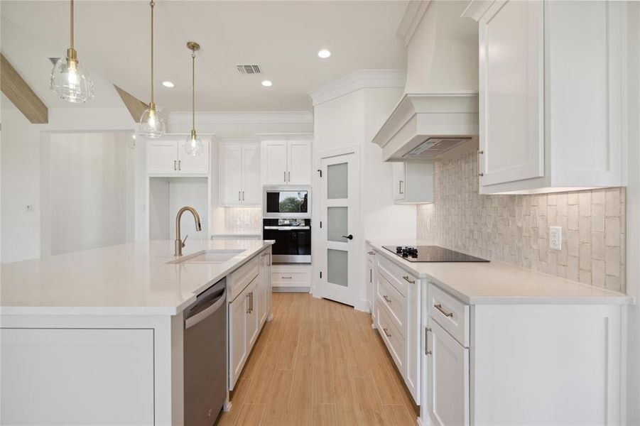 Kitchen with premium range hood, white cabinetry, hanging light fixtures, sink, and dishwasher