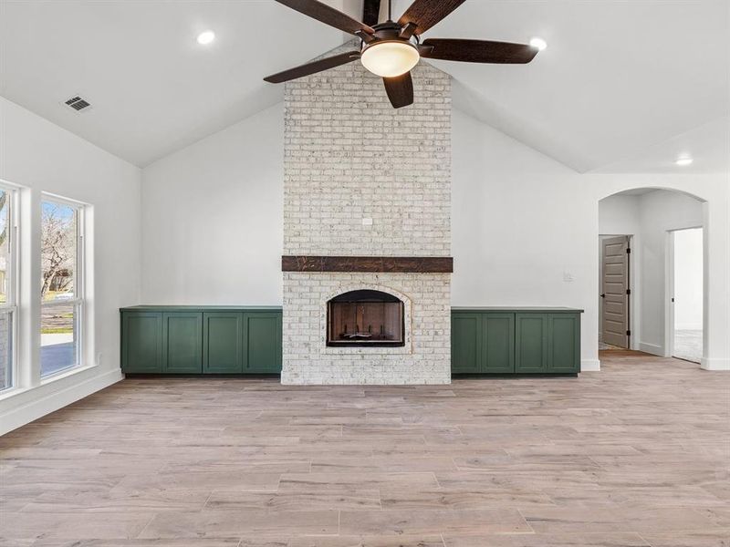 Unfurnished living room with wood finished floors, visible vents, a fireplace, arched walkways, and ceiling fan