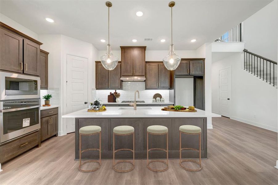 Kitchen featuring an expansive island with a white countertop, recessed lighting, wood-finish flooring, dark wood cabinetry, and stainless steel appliances