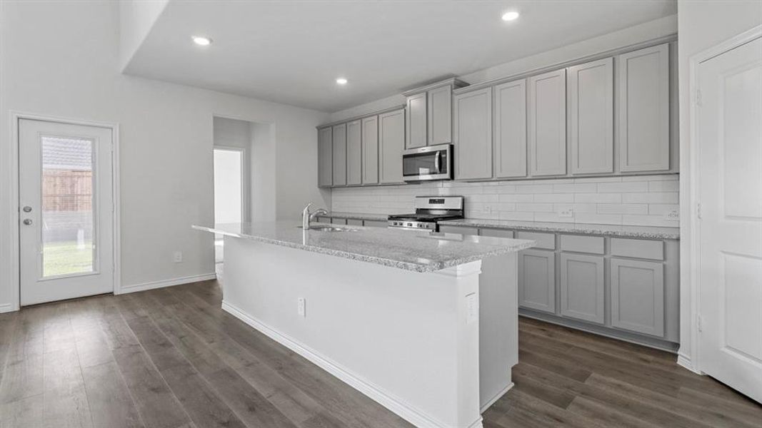 Kitchen with gray cabinets, light stone countertops, appliances with stainless steel finishes, a kitchen island with sink, and recessed lighting