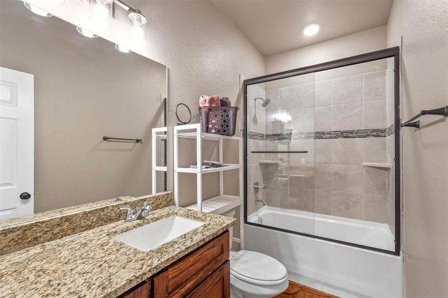 Full bathroom with enclosed tub / shower combo, vanity, and toilet