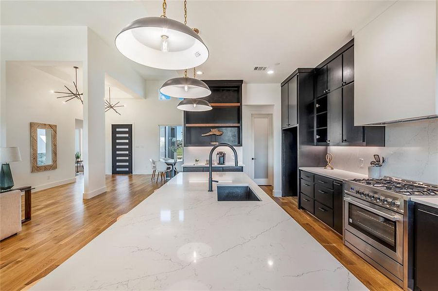 Kitchen featuring light stone countertops, light hardwood / wood-style flooring, decorative light fixtures, sink, and stainless steel range