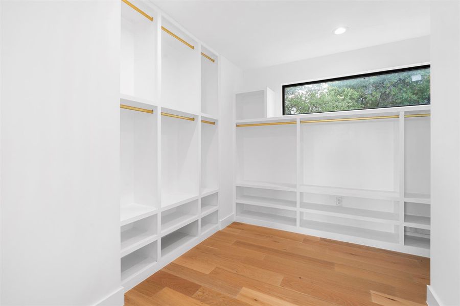 Spacious closet featuring built-in white shelving, gold-toned hanging rods, and hardwood flooring