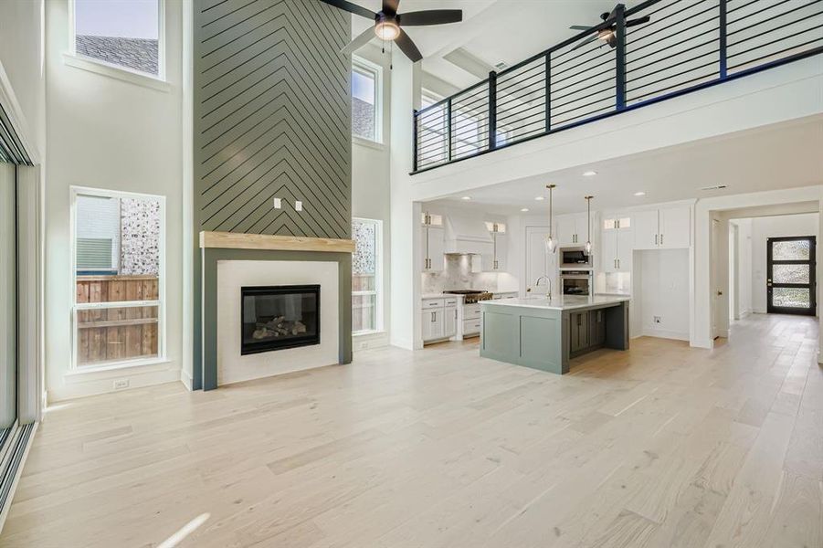 Unfurnished living room with a high ceiling, ceiling fan, light wood-style flooring, and a fireplace Unfurnished living room with a high ceiling, ceiling fan, light wood-style flooring, and a fireplace