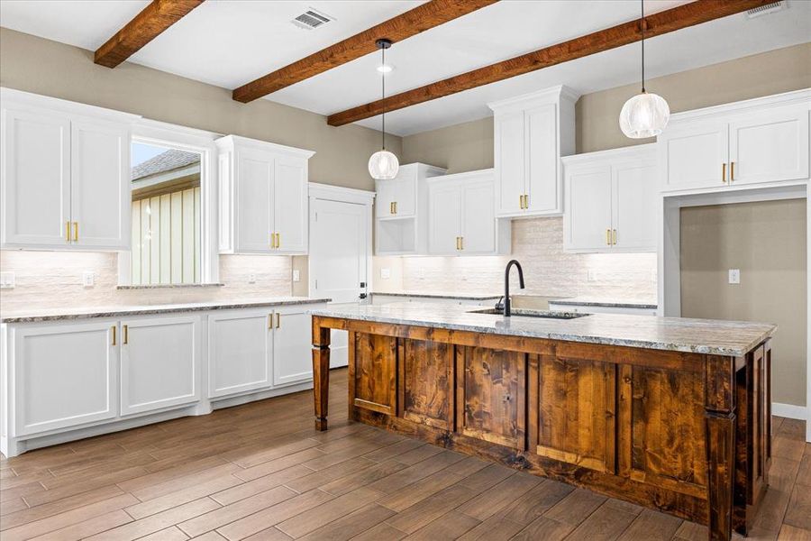 Kitchen with white cabinets, backsplash, a center island with sink, hanging light fixtures, and light stone counters Kitchen with white cabinets, backsplash, a center island with sink, hanging light fixtures, and light stone counters