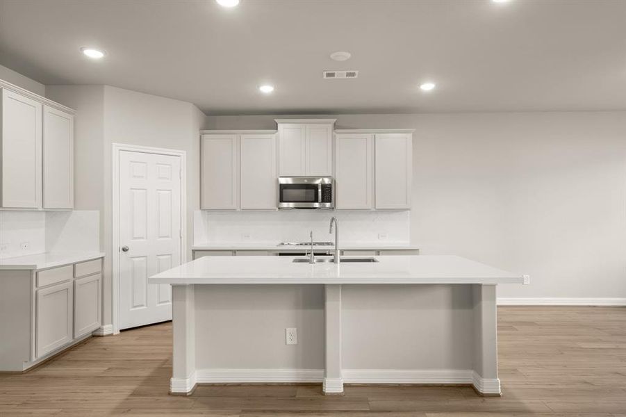 This light and bright kitchen features a large quartz island, white cabinets, a large sink overlooking your family room, recessed lighting, and beautiful backsplash.