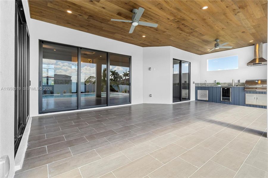 The covered patio features a flat wooden ceiling, an outdoor kitchen, and impact-resistant doors connecting to the living room, formal dining, and master suite.