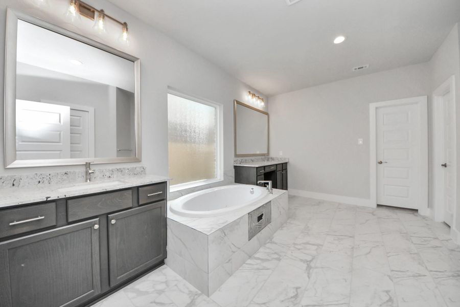 Escape to a spa-like oasis in this primary bathroom. Enjoy a walk-in shower with tile surround, a separate garden tub with custom detailing, and an elegant vanity featuring light countertops, modern hardware, and beautiful vanity lights. Experience luxury and relaxation in every detail.