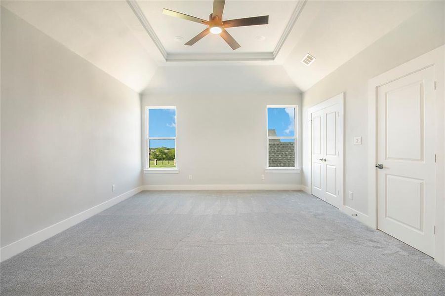 Unfurnished bedroom featuring multiple windows, a raised ceiling, carpet flooring, ornamental molding, and a ceiling fan Unfurnished bedroom featuring multiple windows, a raised ceiling, carpet flooring, ornamental molding, and a ceiling fan