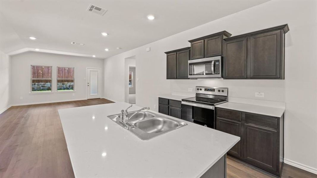 Kitchen island with dual basin sink and stainless steel faucet, dark wood-finish cabinetry, stainless steel microwave, stainless steel electric range, and light countertops