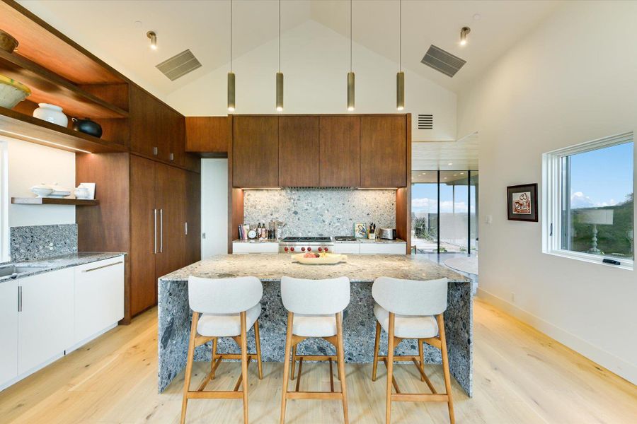 Kitchen with modern cabinets, light wood-type flooring, light stone counters, decorative light fixtures, and high vaulted ceiling