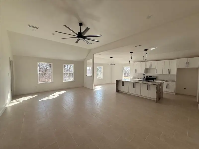 Kitchen featuring open floor plan, white cabinetry, hanging lights, a ceiling fan, and a large island with sink