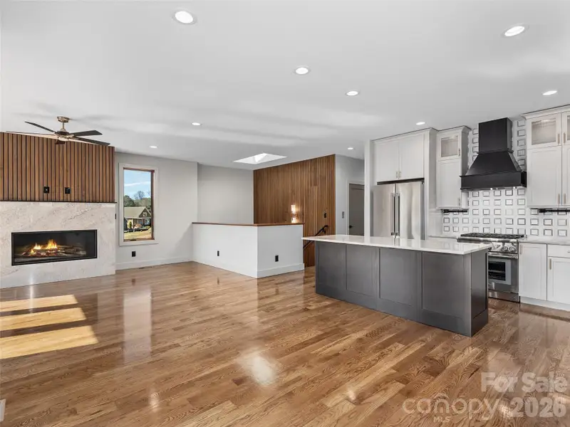 Expansive open-concept main living area featuring oak hardwood floors, vented gas fireplace, designer kitchen with center island, and seamless flow to the stairwell, hall, and elevator access.
