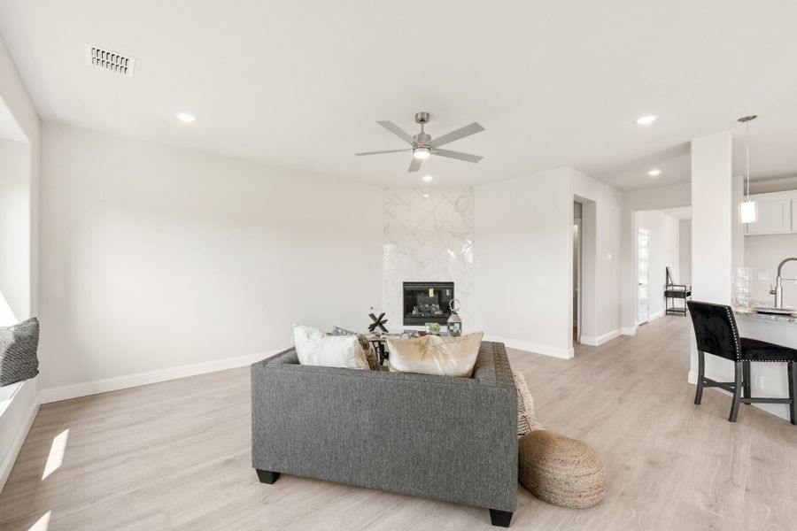 Open living room with gray sofa, marble fireplace, ceiling fan, and light hardwood floors