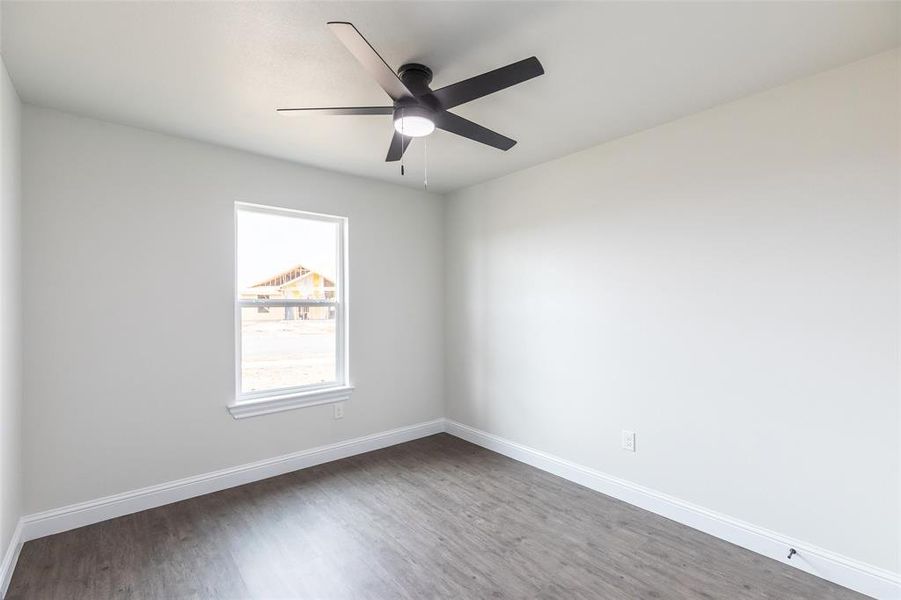 Spacious room featuring wood-finish flooring, white baseboards, and a contemporary black ceiling fan with integrated lighting