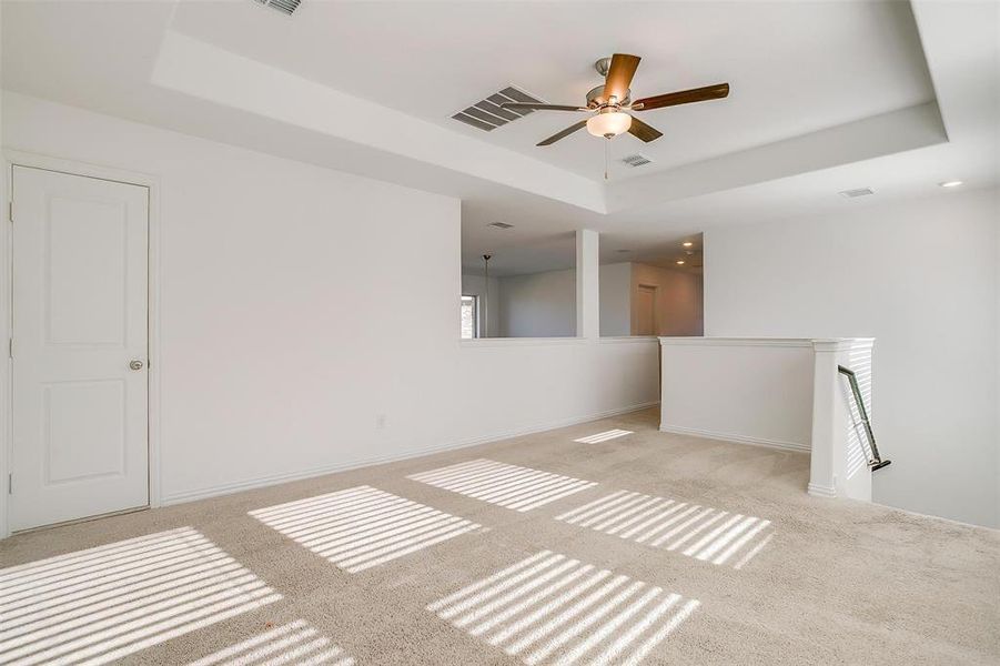 Carpeted empty room with ceiling fan and a raised ceiling