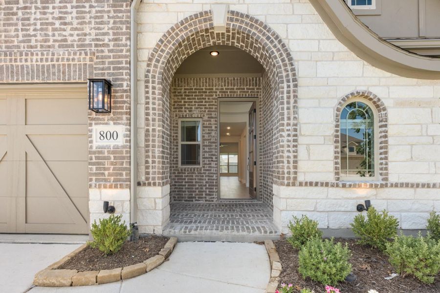 Home entrance with brick arched doorway, stone trim, house number 800, and landscaped walkway