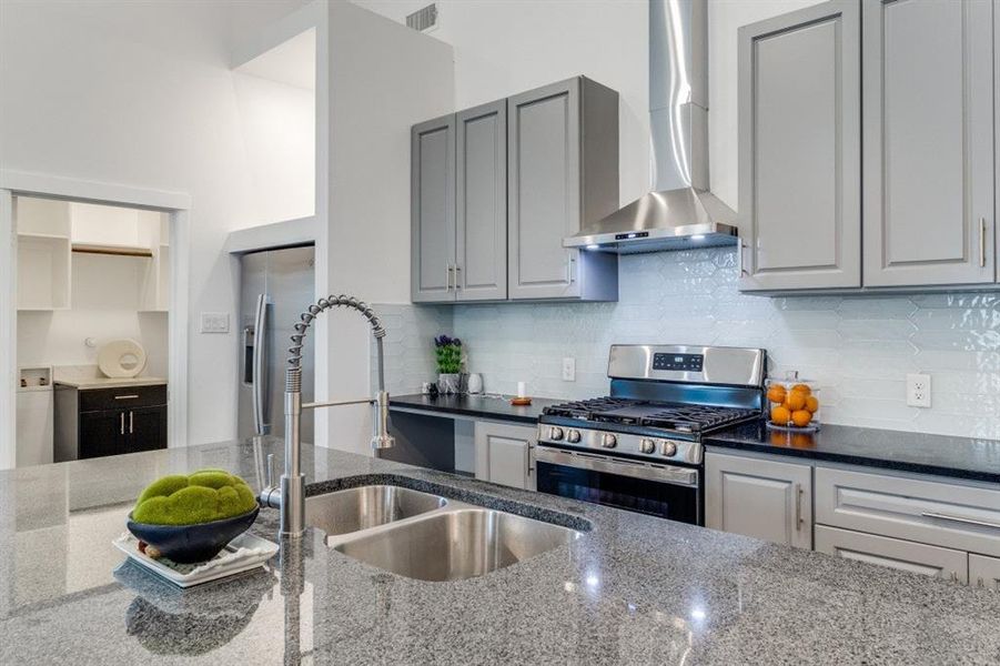 Kitchen featuring appliances with stainless steel finishes, sink, wall chimney exhaust hood, dark stone counters, and gray cabinets