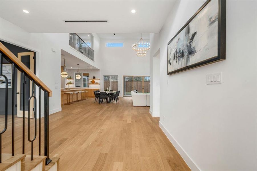 Hall featuring a towering ceiling, light wood finished floors, a chandelier, recessed lighting, and stairs Hall featuring a towering ceiling, light wood finished floors, a chandelier, recessed lighting, and stairs
