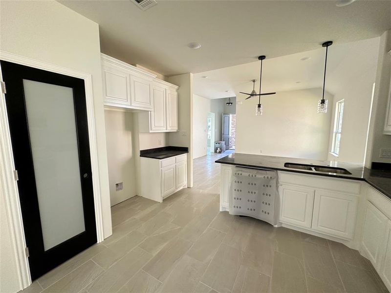 Kitchen with kitchen peninsula, sink, decorative light fixtures, white cabinetry, and ceiling fan