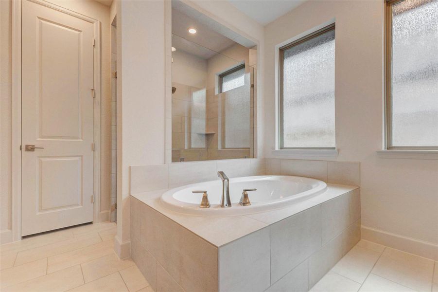 This bathroom features a spacious, modern design with a large soaking tub, neutral tile flooring, and frosted windows for privacy. It offers a serene, spa-like atmosphere. This bathroom features a spacious, modern design with a large soaking tub, neutral tile flooring, and frosted windows for privacy. It offers a serene, spa-like atmosphere.