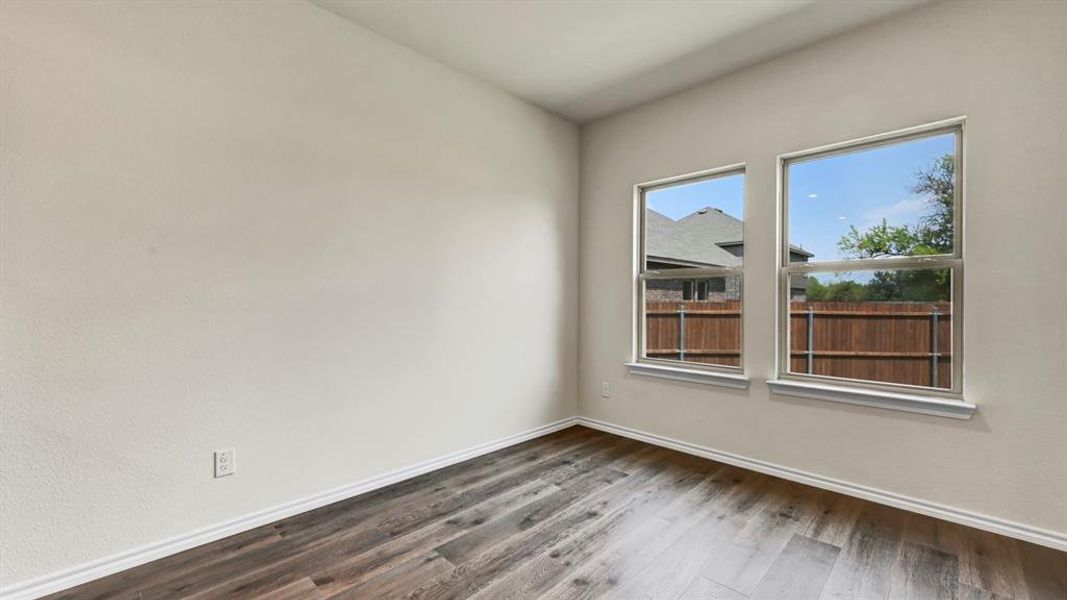 Bright room featuring two windows, wood-finish flooring, and light-toned walls with white trim
