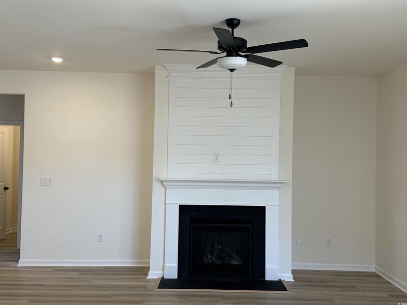 Detailed view of a large fireplace, wood finished floors, ceiling fan, and recessed lighting
