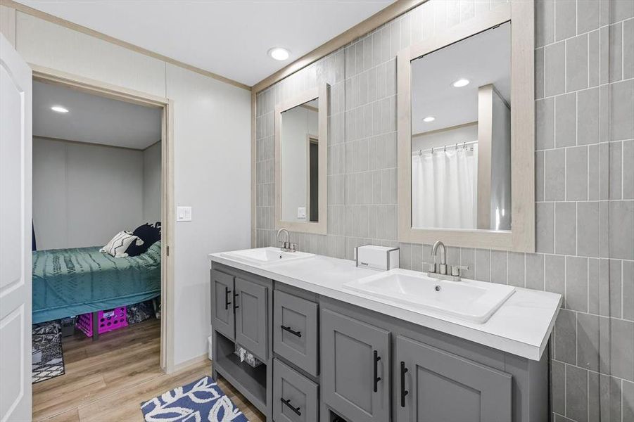 Ensuite bathroom featuring light wood finished floors, recessed lighting, double vanity, and tile walls Ensuite bathroom featuring light wood finished floors, recessed lighting, double vanity, and tile walls