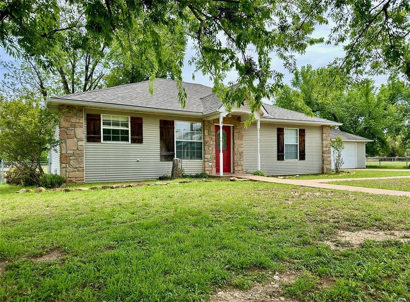 Ranch-style house with stone siding, roof with shingles, and a garage