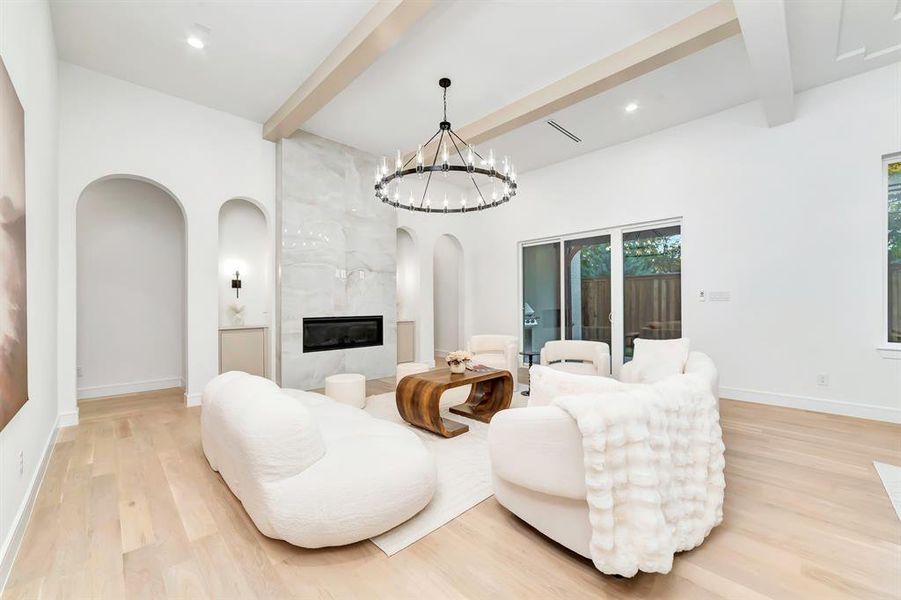 Living area with beamed ceiling, arched walkways, light wood finished floors, a high end fireplace, and a chandelier Living area with beamed ceiling, arched walkways, light wood finished floors, a high end fireplace, and a chandelier