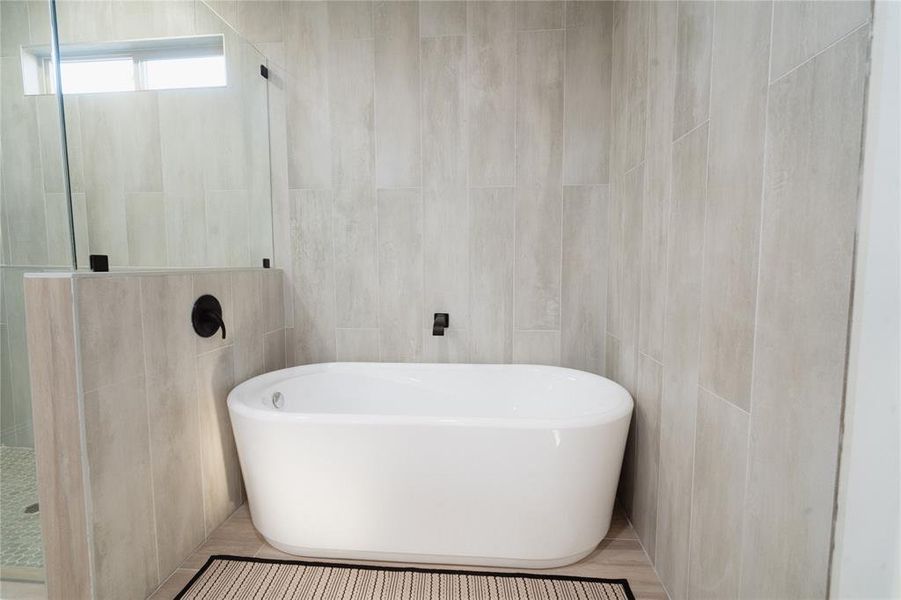 Full bath featuring a freestanding bath, walk in shower, and tile walls