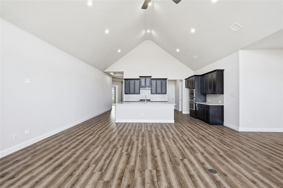 Unfurnished living room featuring a ceiling fan, a high ceiling, and dark wood-style floors Unfurnished living room featuring a ceiling fan, a high ceiling, and dark wood-style floors