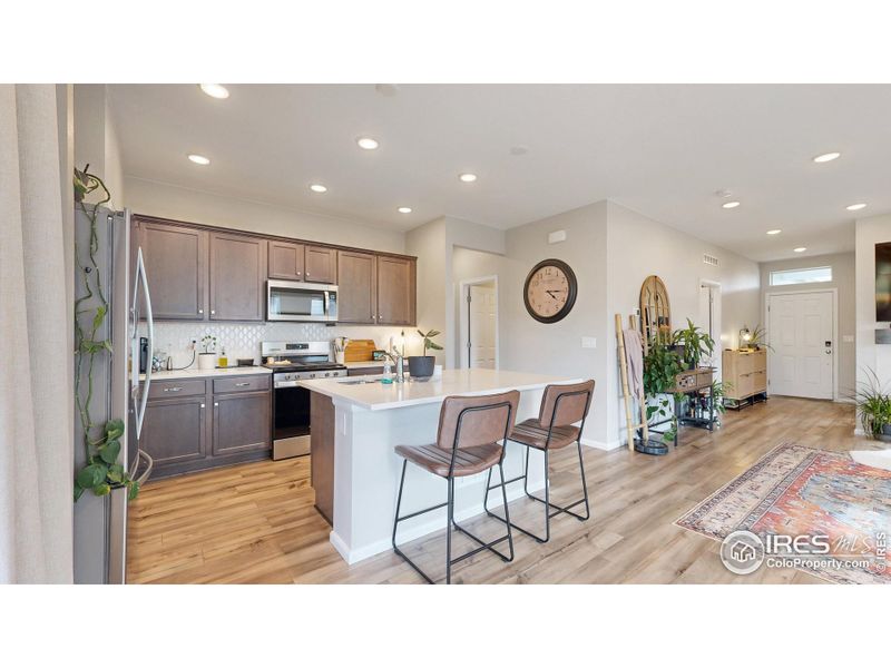 Spacious kitchen featuring stainless steel appliances, a gas range and oven, quartz countertops including a kitchen island and a custom tile backsplash.